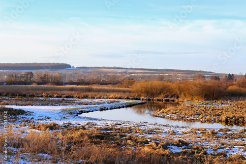 The first snow is a frosty morning. A small river in the grass sprinkled with snow. Golden colors of the morning sun. Rural landscape, Ukraine, Europe.