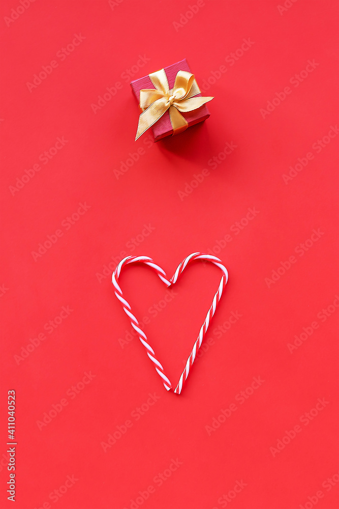 Heart made of Christmas candy cane and gift in a box, Valentine's day concept. Red background, flat lay.