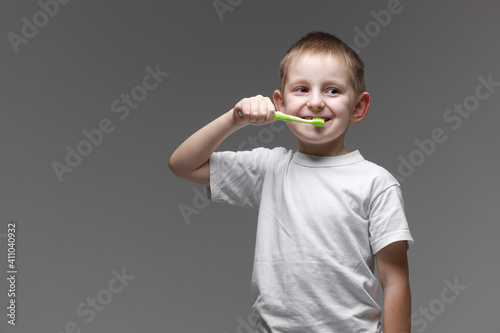 Happy child kid boy brushing teeth with toothbrush on gray background. Health care, dental hygiene. Mockup, copy space photo