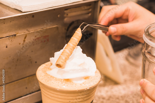 Barista preparing a coffee frappe with whipped cream and a cookie.  2