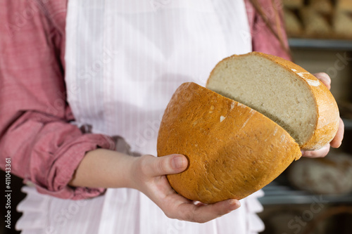 A girl close up shows a round bread cut in half. Two equal parts of wheat bread sliced with a sharp knife.