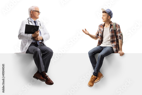 Full length shot of a mature doctor and a teenage male student sitting on a blank panel
