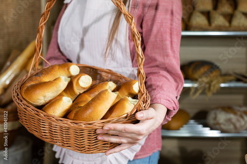 An attractive saleswoman holds fresh buttered croissants in a basket. Family bakery business and flagship store.