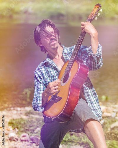 Rock musician man in an open shirt enthusiastically plays the old guitar in nature. Summer, clear day. Retro style, soft light. Musical concept. Portrait, close-up. Instagram size photo.