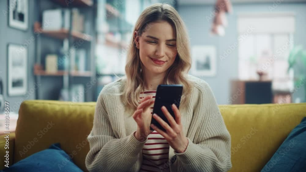 Beautiful Caucasian Female Using Smartphone in Stylish Living Room while Resting on a Cozy Couch Sofa. Young Woman at Home, Browsing Internet, Using Social Networks, Having Fun in Flat. Zoom In Shot.