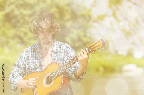 Rock musician man in an open shirt enthusiastically plays the old guitar in nature. Summer, clear day. Retro style, soft light. Musical concept. Portrait, close-up. Bard song.