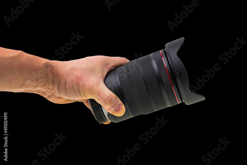 Close up view of male hand holding camera lens isolated on black background.