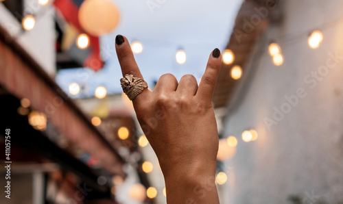 Man's hands with black painted nails, making a rock hand gesture, in the background a Colombian flag, rock al parque