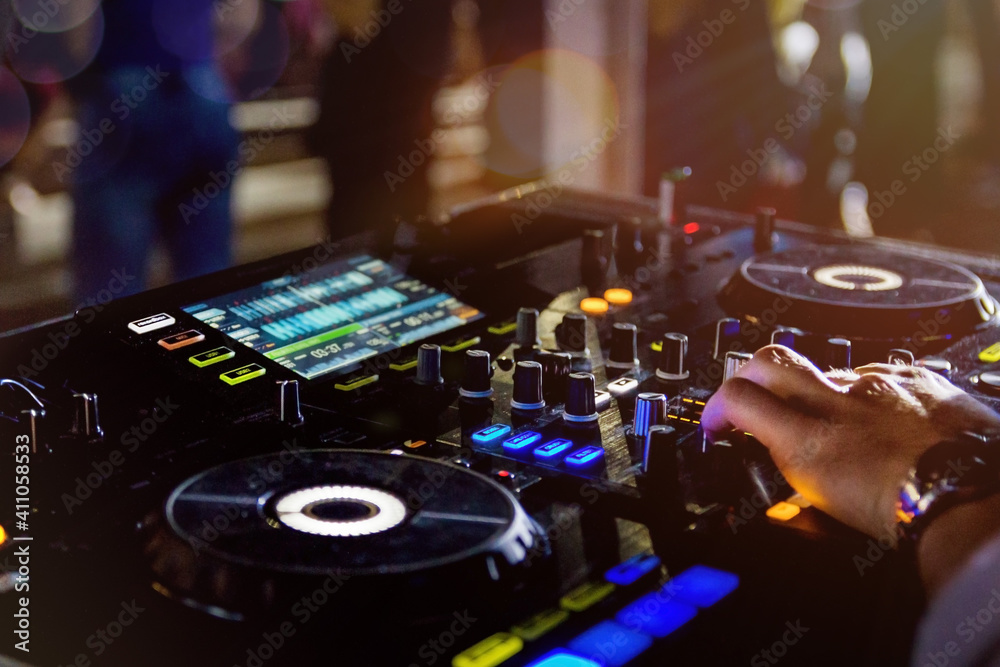 Obraz premium DJ playing music on the record player also knows as a turntable in the night club with light bokeh