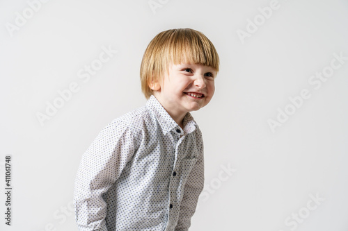 Half length portrait of small caucasian boy standing in front of white wall smiling and looking to the side - little child studio portrait with copy space