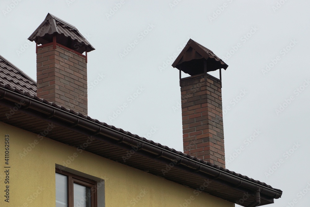 two brown brick chimneys on the roof of a private house against a gray sky