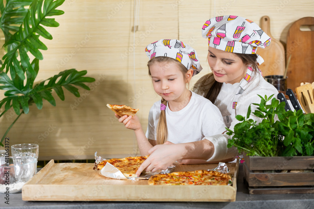 The five-year-old daughter sat down on her mother's lap and together they eat pizza made and baked by themselves. After working together in the kitchen, it's time to eat together. The five-year-old daughter sat down on her mother's lap and together they eat pizza made and baked by themselves. After working together in the kitchen, it's time to eat together.
