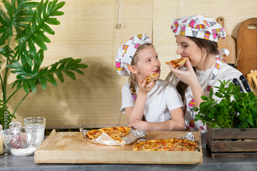 The five-year-old daughter sat down on her mother's lap and together they eat pizza made and baked by themselves. After working together in the kitchen, it's time to eat together.