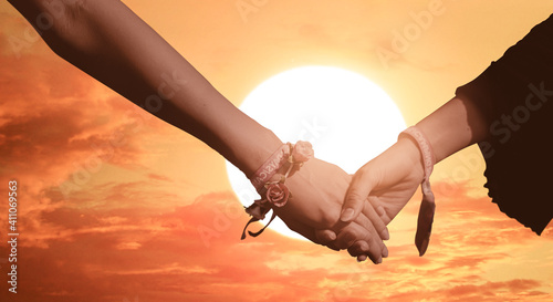 two girls holding hands and against a sunset sky. © Njay