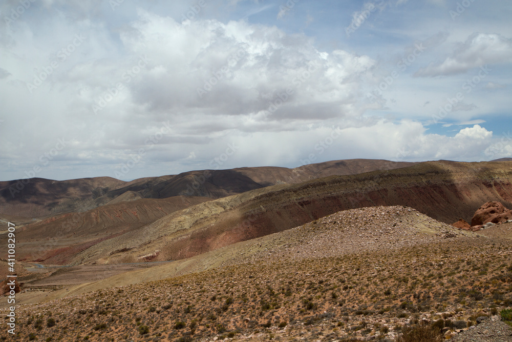 Altiplano desert landscape. Beautiful view of the arid valley meadow, dunes and rocky mountains under a cloudy sky. 