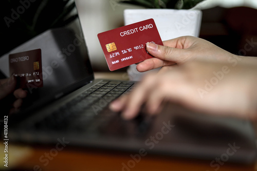 The person holds a red credit card and is filling out their credit card information to pay for goods online, credit cards can pay for goods and services both in the storefront and online shopping.