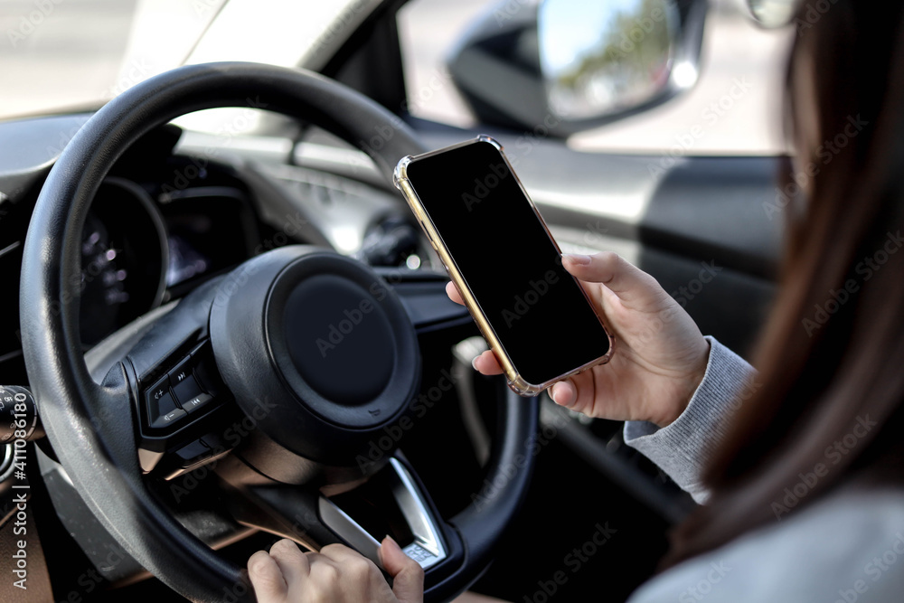 Close-ups of women holding the steering wheel and using mobile phone while driving, using the phone while driving is dangerous and illegal, the concept of safe driving.