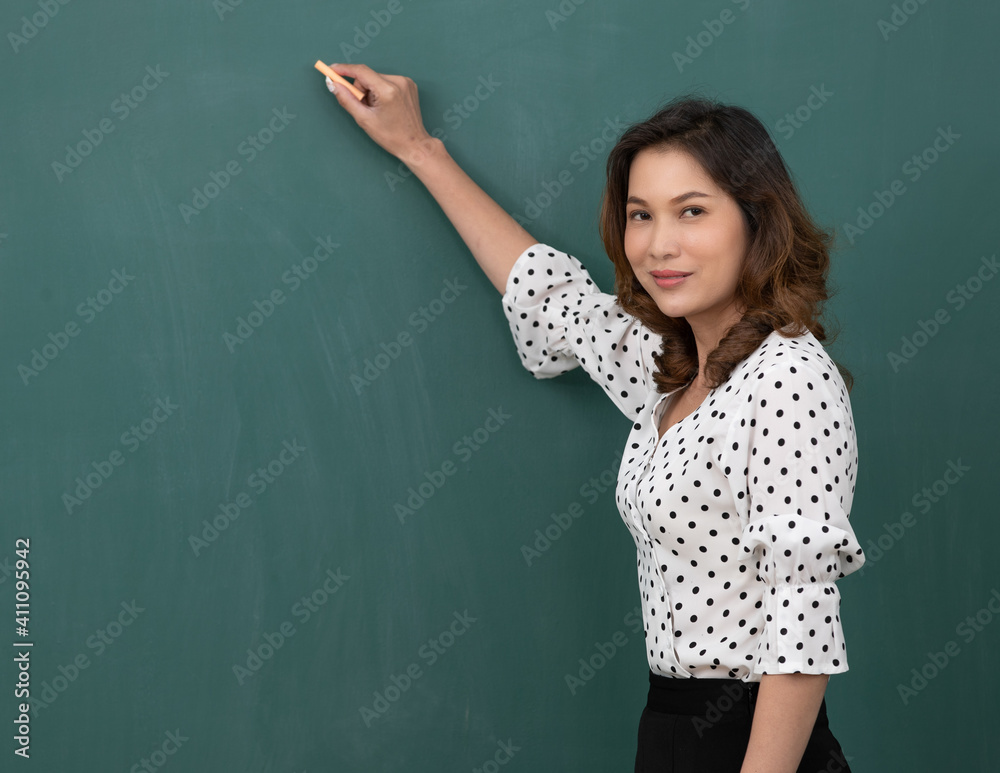 Beautiful Asian woman holding chalk standing in front of black board with copy space
