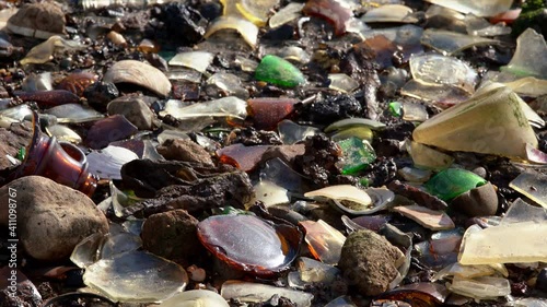 Littered beach in USA. Atlantic Ocean pollution, sandy beach covered by glass and garbage. Trash polluting Nature. Glass Bottle Beach in New York City