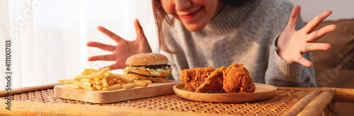 Closeup image of a young woman happy to eat hamburger, french fries and fried chicken on the table at home