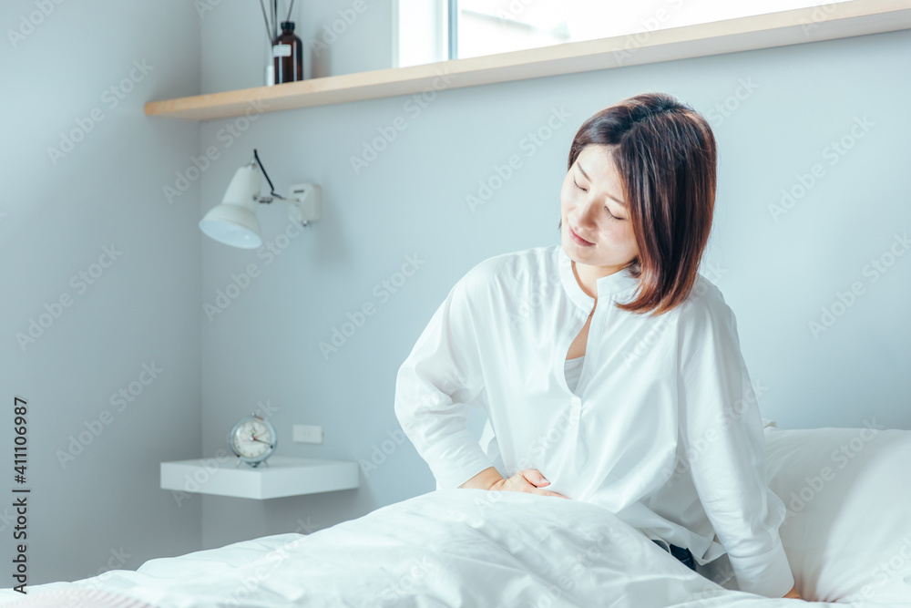30代女性が綺麗なベットの上で朝起きてお腹が痛い　
