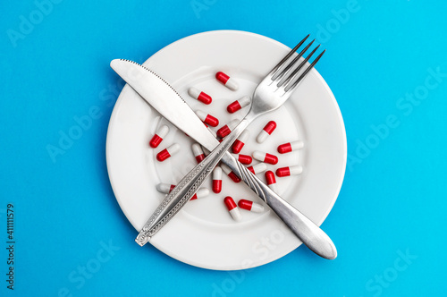 Red-white pills on the plate with fork and knife. Diet. Healthy lifestyles.