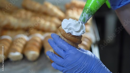 A woman fills the horns with cream from a pastry bag. Hands in gloves close up photo