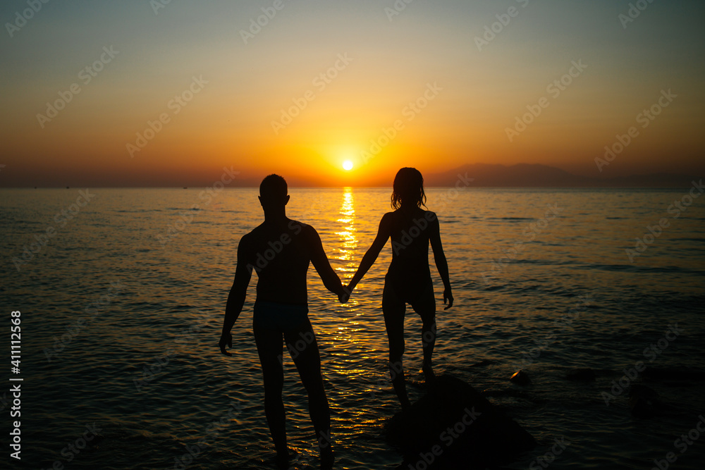 Romantic couple on the beach watching on sunset in twilight. Silhouette.