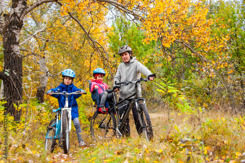 Family cycling in golden autumn park, active father and kids ride bikes, family sport and fitness with children outdoors 