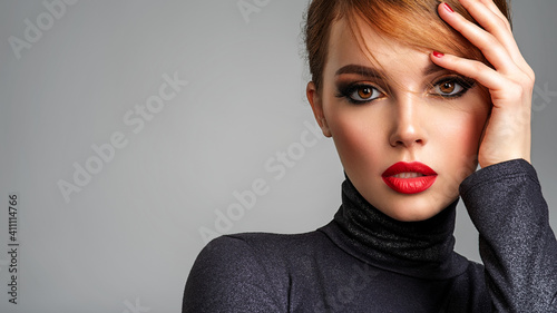 Beautiful brunette girl with red lips and short, slick hair. Pretty young sensual woman with red nails. Closeup portrait of a model with bright makeup on a face. Attractive female posing at studio.