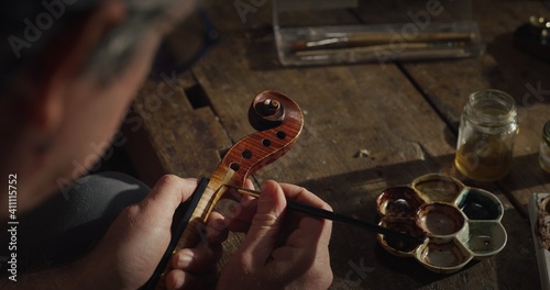 Cinematic shot of experienced master artisan luthier painstaking detail work on fine quality wood violin in creative workshop.Concept of spiritual instrument,handmade, art, orchestra, artisan, passion