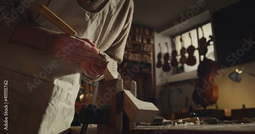 Cinematic shot of experienced master artisan luthier painstaking detail work on fine quality wood violin in creative workshop.Concept of spiritual instrument,handmade, art, orchestra, artisan,passion photo