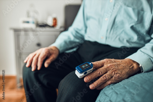 Senior man measuring the degree of oxygen saturation of the blood and heart rate at home using pulse oximeter. Home treatment of virus. Checking health condition. Coronavirus pandemic