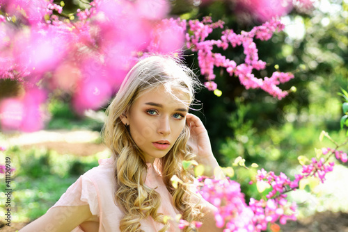 Young woman enjoy flowers in garden. Girl walks in park on sunny spring day.