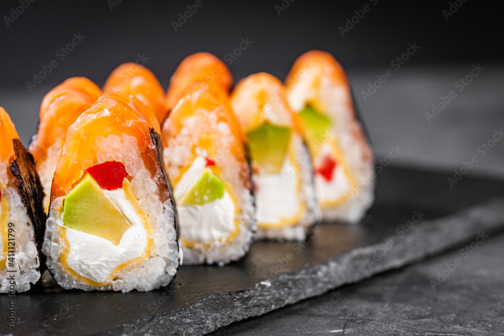 appetizing sushi roll philadelphia with avocado cheese omelette and salmon on a black stone plate appetizing sushi roll philadelphia with avocado cheese omelette and salmon on a black stone plate