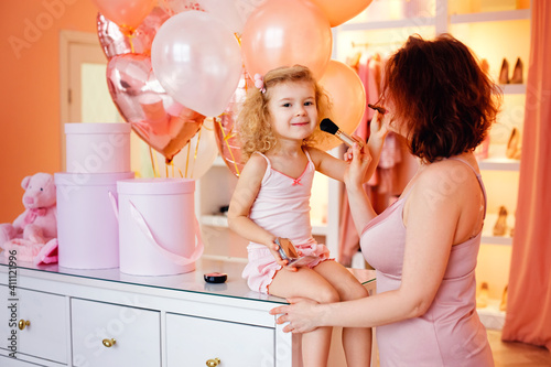 A happy, loving family. Mother and daughter doing your makeup and having fun. Mom and girl in pajamas in a pink room with balloons. Mother's Day concept.