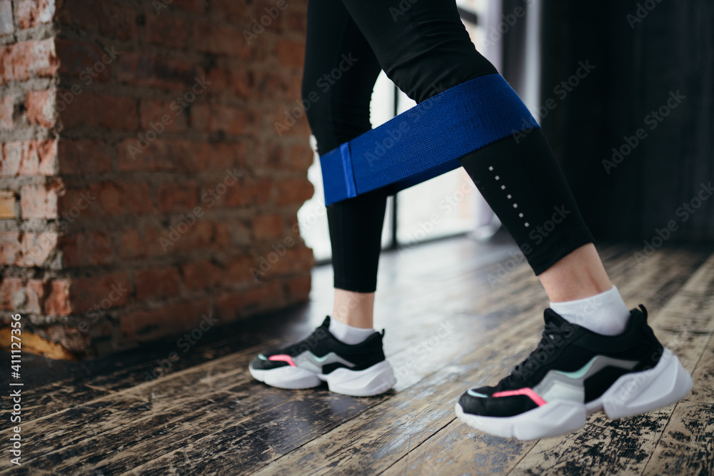 Trainer in black leggings leaned against the wall and performs the exercise using a sports elastic band Trainer in black leggings leaned against the wall and performs the exercise using a sports elastic band