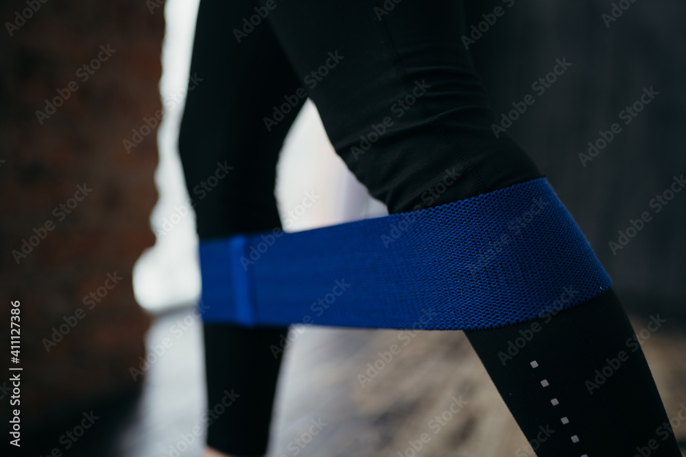 Trainer in black leggings leaned against the wall and performs the exercise using a sports elastic band Trainer in black leggings leaned against the wall and performs the exercise using a sports elastic band