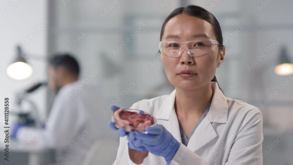 Slow-motion close up portrait of female Asian microbiologist examining petri dish with artificial cultured meat sample Slow-motion close up portrait of female Asian microbiologist examining petri dish with artificial cultured meat sample