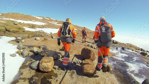 A group of polar explorers in orange suits and backpacks are walking across Antarctica. Video of scientist research group look at the South Pole. 