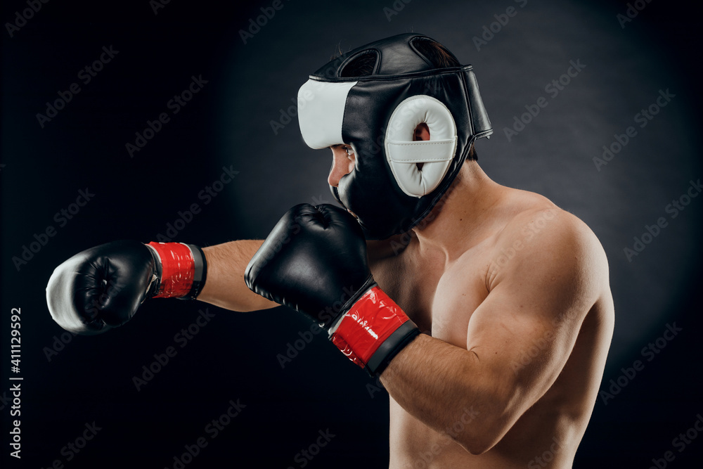 Portrait of a young man with a Boxing helmet and gloves on a dark background.