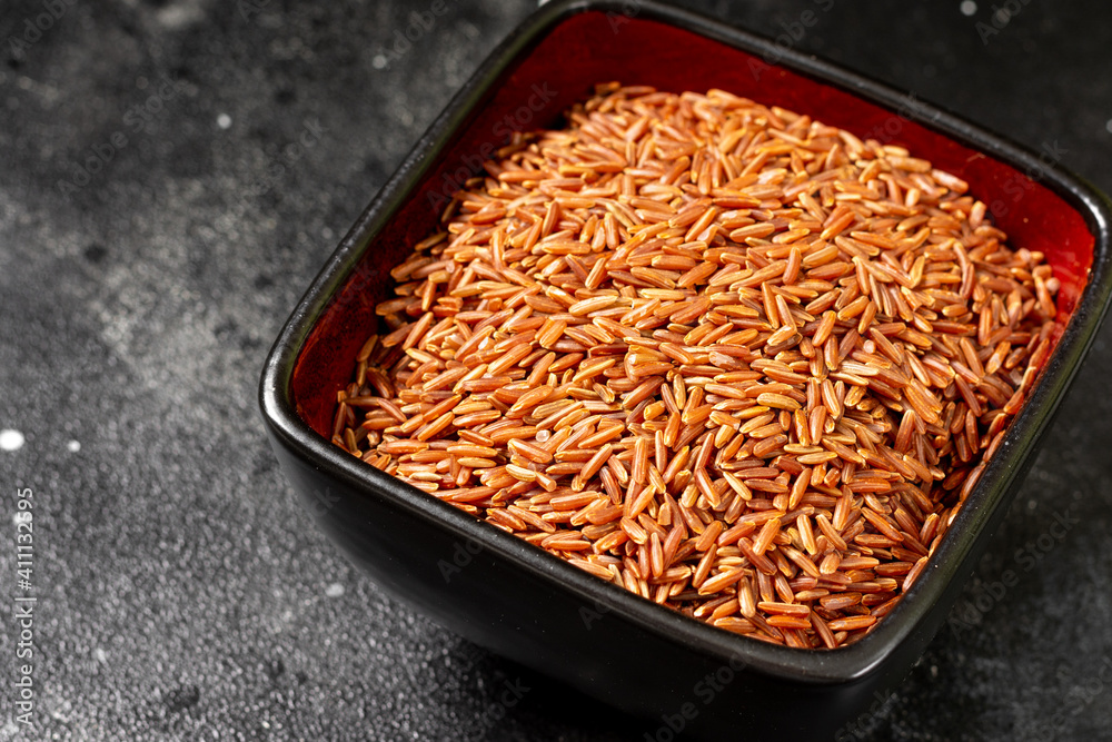 Red mlm brown rice in a ceramic bowl on a black kitchen table. Red rice on a dark background Red mlm brown rice in a ceramic bowl on a black kitchen table. Red rice on a dark background