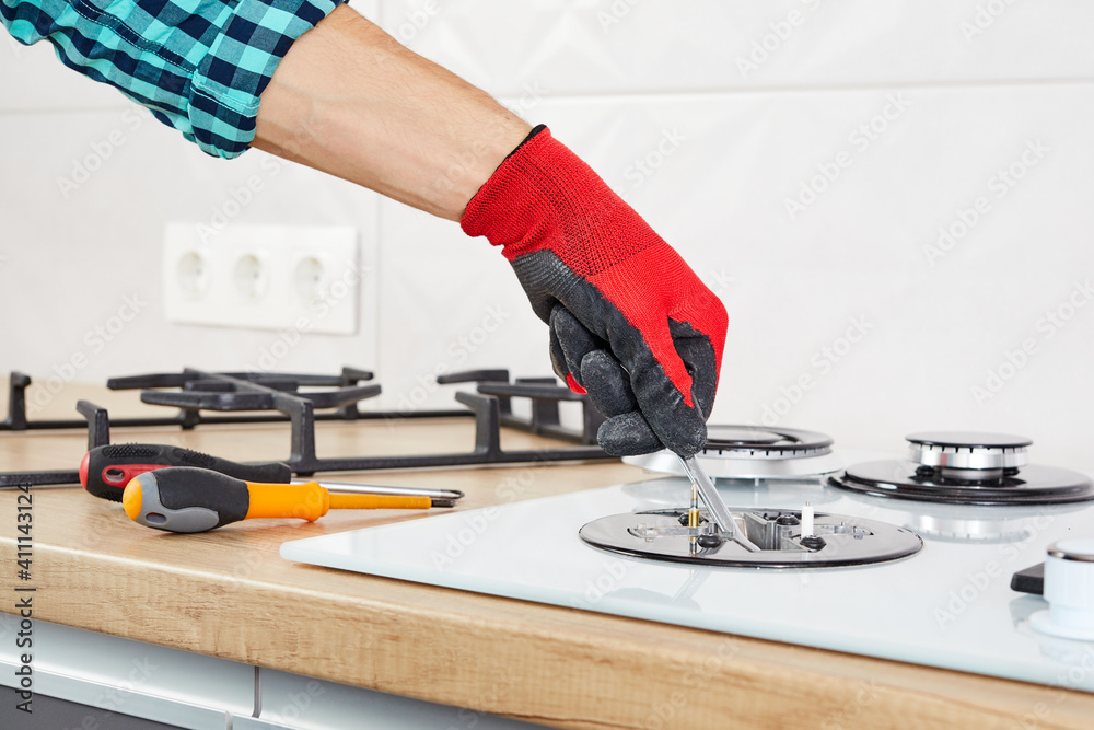 Repairs and fixing of gas control panel. Man hand in protective gloves repairs hotplate of hob. Repairs and fixing of gas control panel. Man hand in protective gloves repairs hotplate of hob.