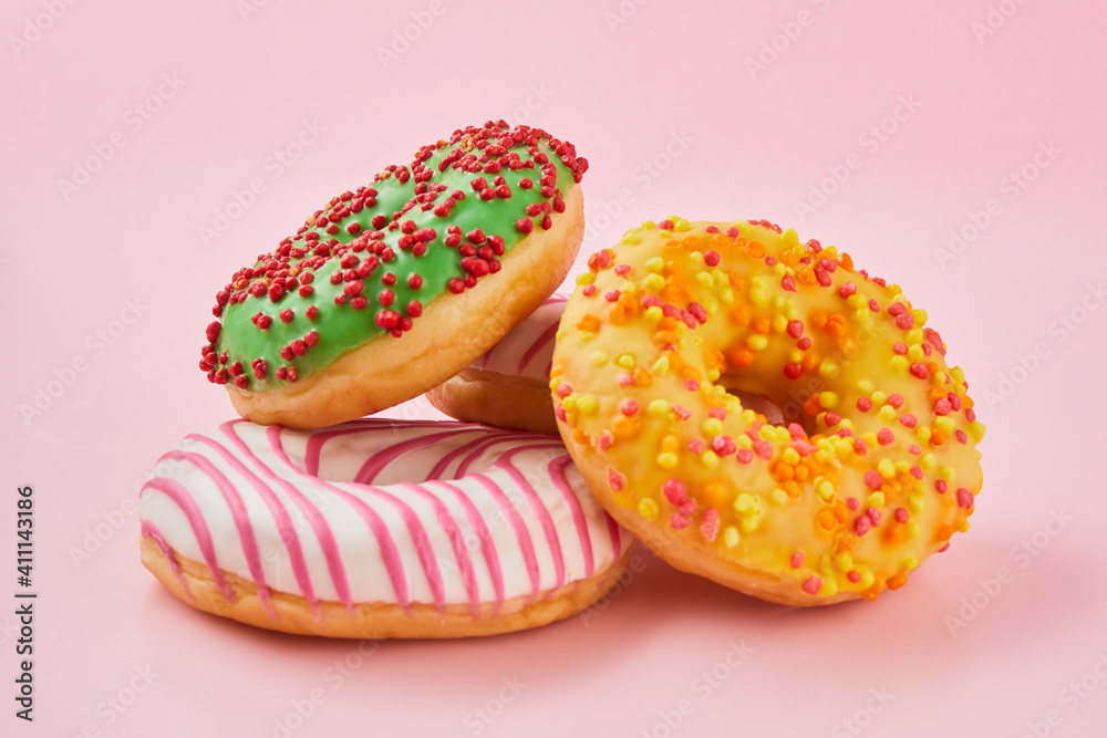 Doughnut with multicolored glaze on trendy pink background. Donut are traditional sweet pastries.