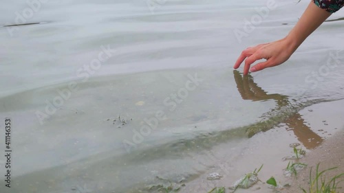 The girl touches the water on the river with her fingers. Close-up shot of a woman's hand on a background of water by the lake. photo