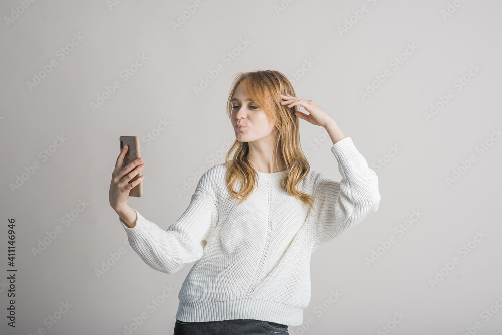 Beautiful young girl on a white background in the studio makes a selfie on a smartphone Beautiful young girl on a white background in the studio makes a selfie on a smartphone