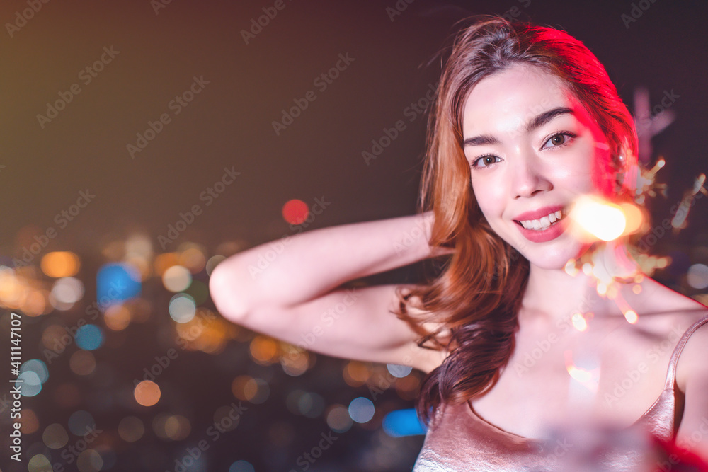 Beautiful young asian brunette woman with white dress joying Christmas or New Year night on a city.Woman holding sparkler against defocused lights, close up. Beautiful young asian brunette woman with white dress joying Christmas or New Year night on a city.Woman holding sparkler against defocused lights, close up.