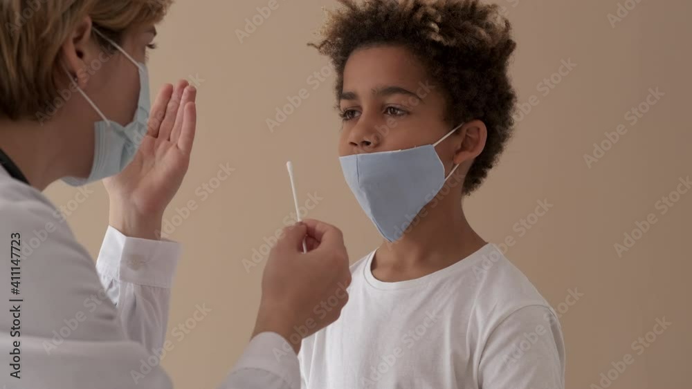 Female practitioner doctor takes nose swab of 10s patient. Little mixed-race boy pass PCR or polymerase chain reaction test for diagnosing of COVID-19 pandemic infection. Medical check up concept