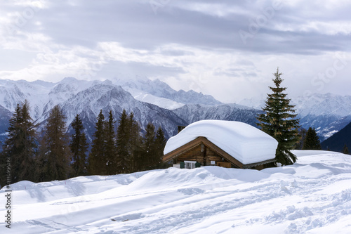 Alpine chalet sunk in deep snow in winter with thick snow on roof in the Swiss Alps, Switzerland