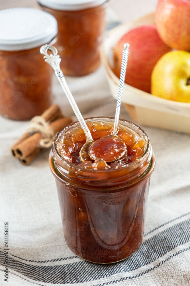 Homemade apple jam marmalade with cloves and cinnamon from organic apples in a transparent glass jar with two vintage retro spoon. Homemade autumn jam preserves.